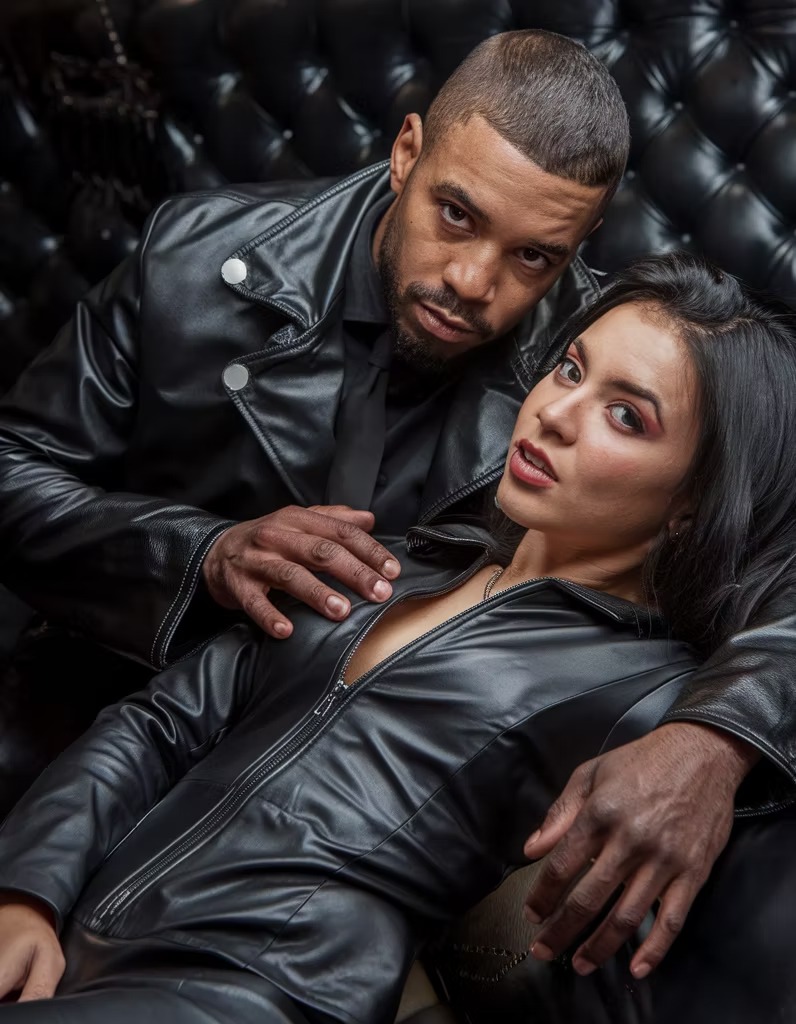 A couple in leather lounging on a tufted black chesterfield
